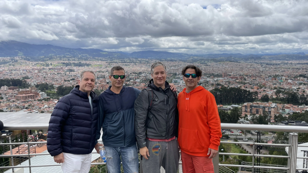 Four brothers standing together on a scenic overlook above Cuenca, Ecuador, with the city and Andean mountains visible under cloudy skies.